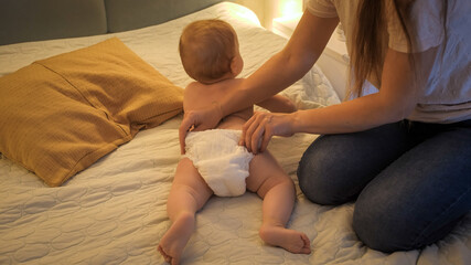 Mother changing messy used diapers to her baby son at night. Concept of children hygiene,...