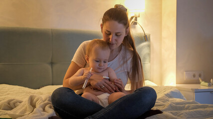 Obraz premium Worried mother checking body temperature of her sick baby son awake at night