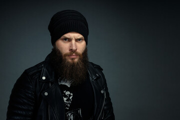 portrait of handsome bearded man in leather jacket and hat looking at the camera