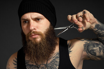 portrait of a courageous man with a beard he holds scissors near his beard and looks at the camera