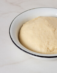 Homemade freshly cooked yeast dough in white bowl on marble table