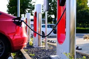Tesla red passenger electric car replenishes battery at charging station, alternative energy development concept, electric vehicle production