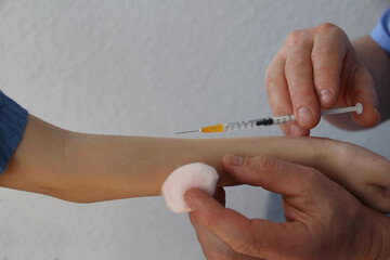 male doctor, nurse in blue uniform makes an injection with a syringe to boy 8-10 years old, close-up hand of child, medical concept, vaccination against the covid-19 virus