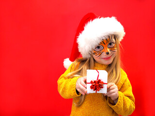 Child girl blonde in a Santa hat and a tiger mask holding a present in her hands. Year of the tiger.  Symbol of the year.  New Year.