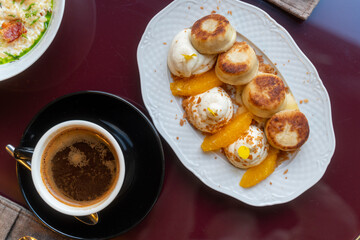 Sweet morning breakfast in cafe. Cheesecakes with cream and peaches, cup of dark coffee