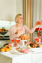 A lovely 40-year-old woman is sitting at a festive table, smiling and holding a glass of wine in her hand. Christmas Holiday, Thanksgiving Day, New Year.