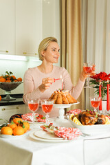 A lovely 40-year-old woman is sitting at a festive table, smiling and holding a glass of wine in her hand. Christmas Holiday, Thanksgiving Day, New Year.