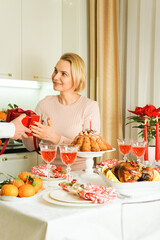 A nice 40-year-old woman is sitting at a festive table, smiling and receiving a gift. Christmas Holiday, Thanksgiving Day, New Year. Festive red gift box.