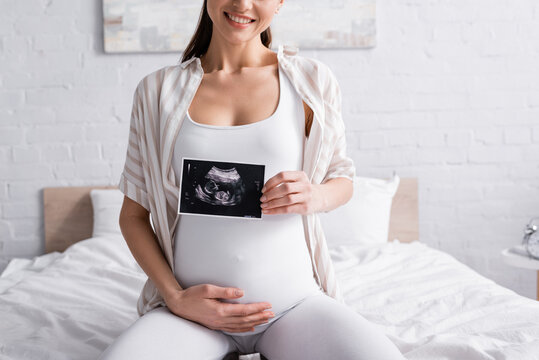 partial view of cheerful pregnant woman holding ultrasound scan.