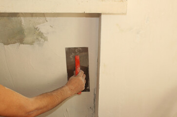 Close-up of a man's hands with a putty knife applying putty to the wall under the window. Cover the...