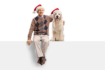 Elderly man with a labrador retriever dog wearing christmas santa hats and sitting on a panel