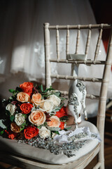 The bride's bouquet Beautiful bouquet of white orange and red roses and greenery lies on a white vintage wooden chair Fresh colorful bouquet of mixed roses White lace wedding dress on the background 