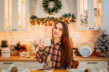 girl sitting in the christmas decorated kitchen and drinking coffee 