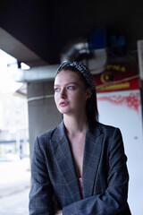 Portrait of white blond young woman with a ponytail in grey jacket with blue eyes in an industrial area