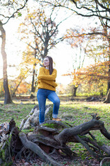 European white young woman in yellow sweater in sunny autumn forest standing on tree roots