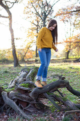 Young european white woman in yellow sweater in sunny autumn forest looking down on tree roots