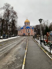 Pink Temple of the Russian Orthodox Church with a golden dome in a cemetery in November against a gray sky