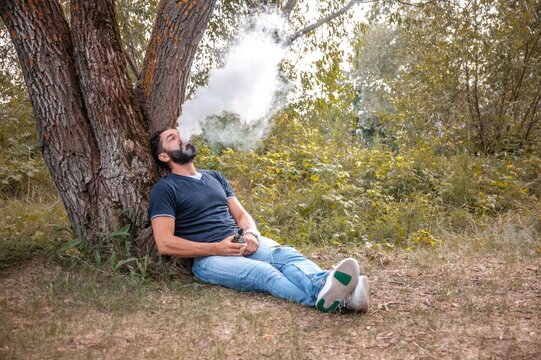 Stylish brutal vape man vaping an electronic cigarette out in the forest. Health concept.