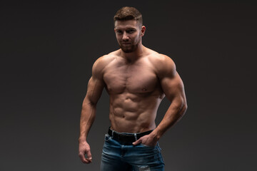 Fototapeta na wymiar Waist up portrait view of the bodybuilder posing and showing his muscle definition. Man in good shape against dark background