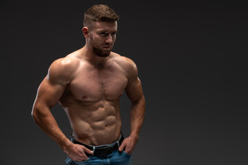 Fototapeta na wymiar Waist up portrait view of the bodybuilder in good shape against dark background. Man posing and showing his muscle definition