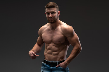 Fototapeta na wymiar Waist up portrait of bearded shirtless bodybuilder looking at the camera while posing over the black wall. Stock photo
