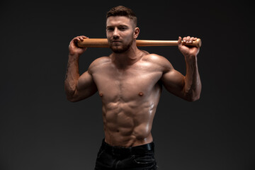 Strong and fit man bodybuilder with baseball bat shows abdominal muscles. Sporty muscular guy...