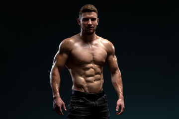 Young handsome male athlete showing muscles isolated on a dark background. Sport and bodybuilding...