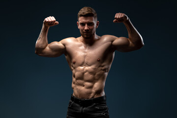 Fototapeta na wymiar Young handsome male athlete showing muscles isolated on a dark background. Sport and bodybuilding concept