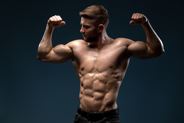 Young athletic man with a naked torso showing his biceps isolated on a dark blue background....