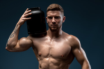 Fototapeta premium Waist up portrait of sporty handsome man with naked torso holding bottle with healthy protein drink, isolated over black studio background