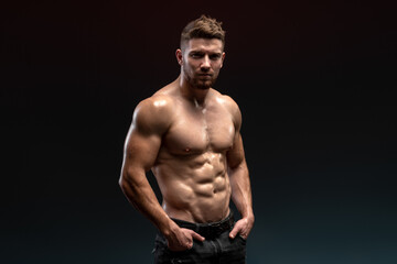 Horizontal view of the handsome muscular guy posing isolated on black background, while showing his...