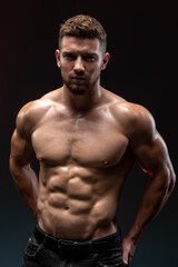 Fototapeta na wymiar Vertical shot of the handsome muscular guy posing isolated on black background, while showing his strong body and muscles