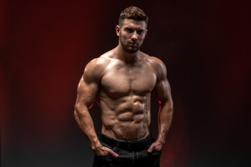 Fitness model showing his perfect body isolated on dark background. Bodybuilder man with perfect abs, shoulders, biceps, triceps and chest. Strong athletic man concept