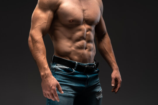 Cropped studio shot of young handsome caucasian man showing his abs and posing against black background. Stock photo