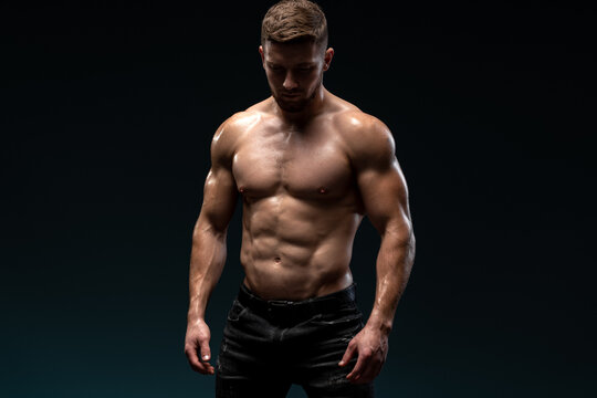 Bodybuilder posing on black background. Beautiful sporty guy male power. Fitness muscled man standing at the studio