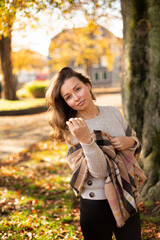 Fototapeta na wymiar European white young woman with brown hair with warm autumn scarf near the tree