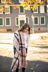 Walking young woman with brown curly hair in warm scarf in autumn city