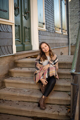 Sitting young woman with curly hair wrapped in a scarf near old building with stairs