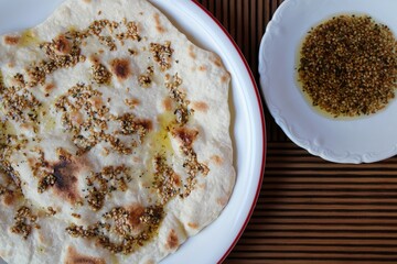 Traditional flatbread with olive oil, sesame seeds and herbs on a wooden background