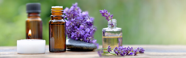 bottles of essential oil among lavender flowers arranged on a wooden table with canddle and pebble