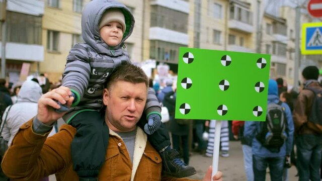 Single father and boy kid with chroma key green screen mock up banner. People at city streets political demonstration. Dad with empty blank banner. Protest family with tracking points sign at rally.