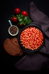 Traditional Greek dish, white beans in tomato sauce, top view, on a black background, no people, vertical, toned,