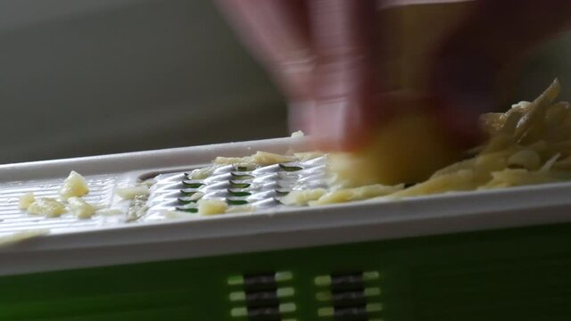 Male hands rubbing potatoes on a kitchen grater for vegetarian food cooking