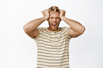 Portrait of frustrated upset man holding hands on head, shouting desperate. Guy with headache suffering huge pain, white background
