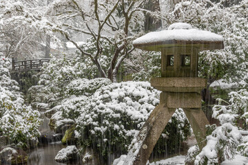 Portland, Oregon. Snow-covered Harp stone lantern and Moon bridge, Portland Japanese Garden.