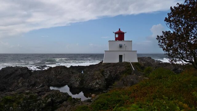 View of Amphitrite Point Lighthouse in small town Ucluelet on Vancouver Island in British Columbia, Canada on cloudy day in autumn season with rugged rocks and rough sea with strong surf.