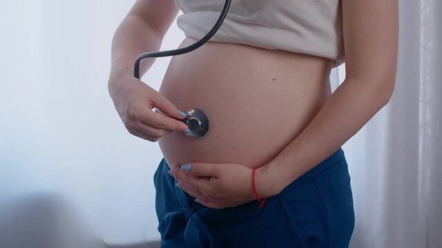 Pregnant woman with stethoscope trying to hear her baby heartbeat at home. Woman with tammy preparing for the birth of the baby.