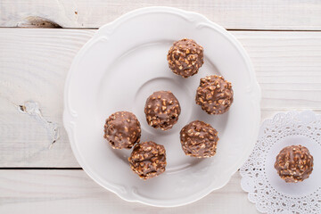 Several sweet chocolates with nuts with ceramic dishes on a wooden table, close-up, top view.