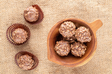 Several sweet chocolates with nuts in a wooden cup on burlap, close-up, top view.