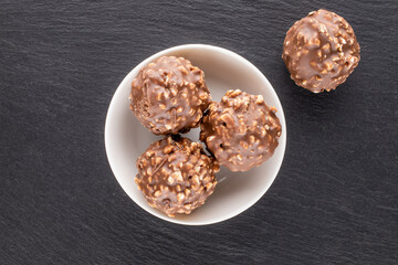 Four sweet chocolates with nuts with a ceramic saucer on a slate stone, close-up, top view.